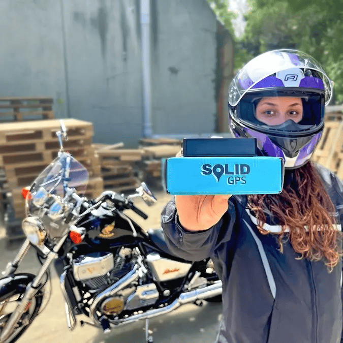 Woman showing a Solid GPS tracker in front of a parked motorcycle